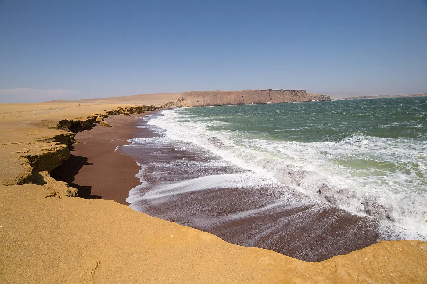 Red sand, ochre cliffs, and surf at Playa Roja in the Paracas National Reserve